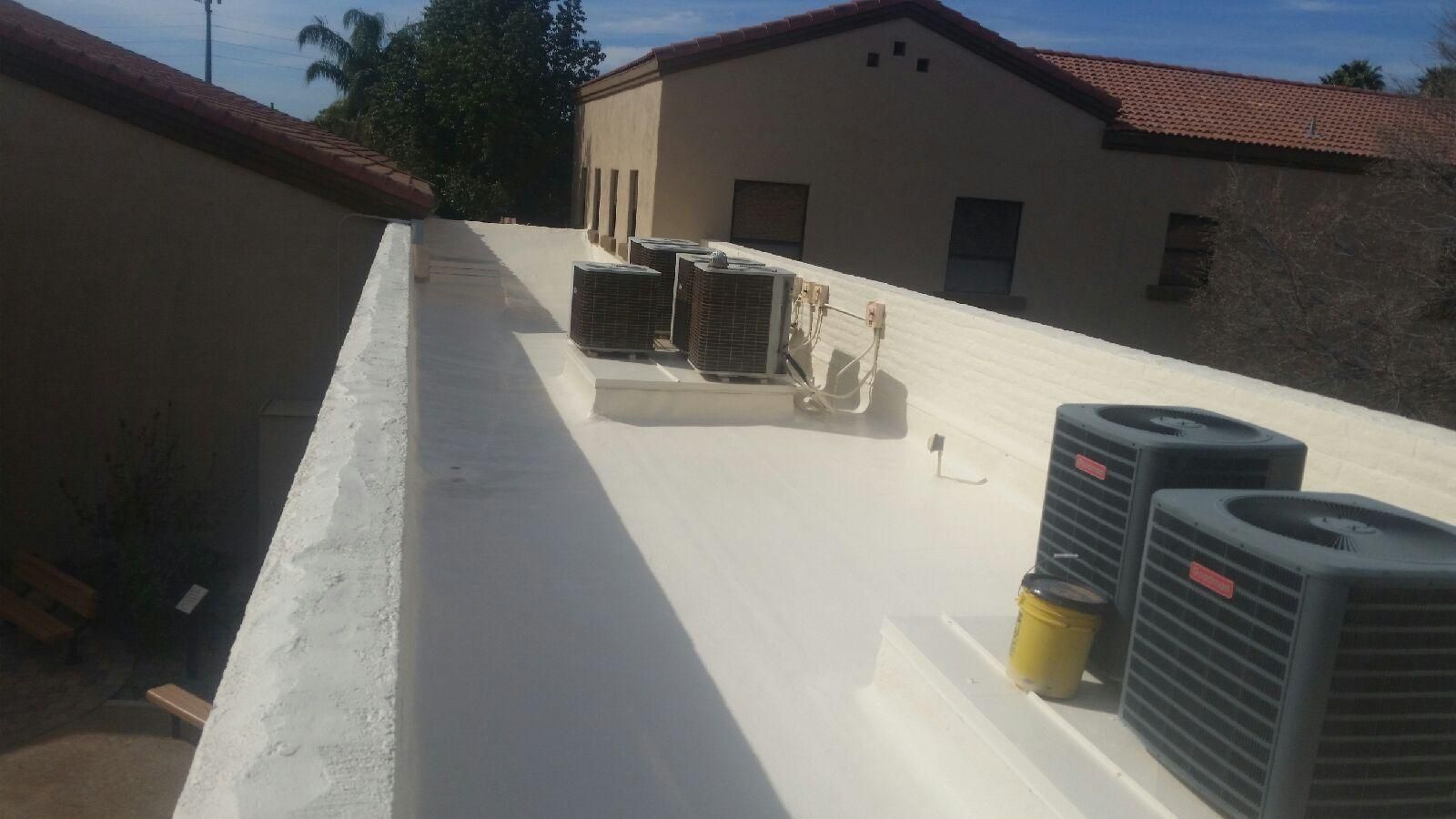 Rooftop with HVAC units and ductwork on a white flat roof beside a tan building under clear skies