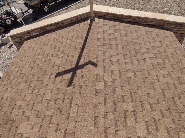 Rooftop with tan shingles and a shadow of a pole cast across the surface