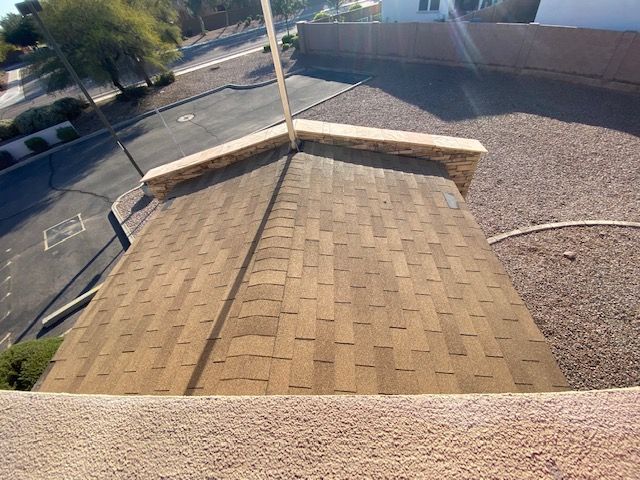 Rooftop with tan shingles, gravel area, and street view beyond a low brick wall.