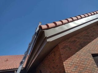 Close-up of a brick house roof with red tiles and a gutter under a clear blue sky