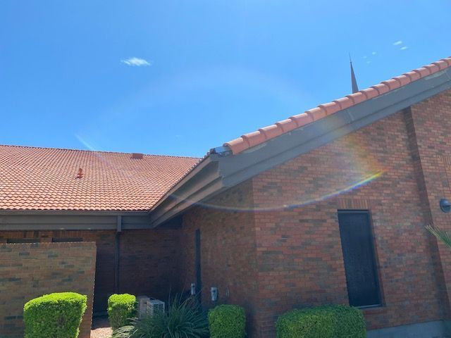 Brick house with red-tiled roof under a clear blue sky, sunlight flaring across the front porch.