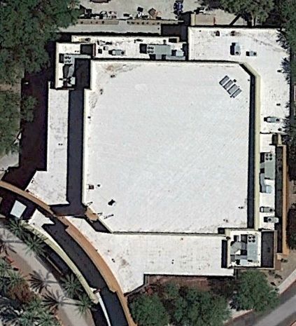 Aerial view of a large white-roofed building with surrounding roads and trees.