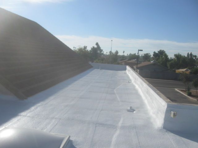 White flat rooftop under blue sky, with nearby trees and buildings in the background.