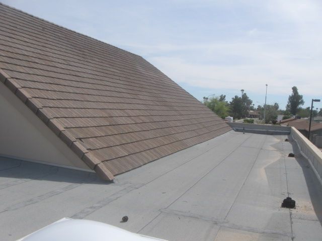 Flat rooftop with gray membrane and a sloped shingled section under a clear sky