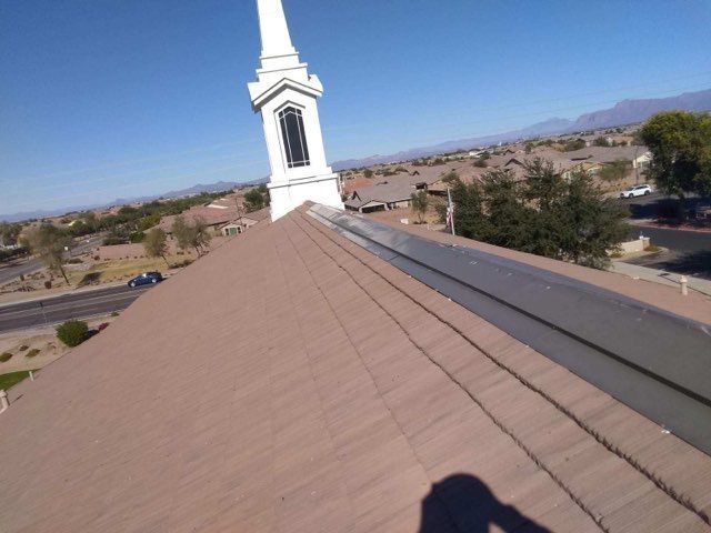 View from a sloped church roof with a white steeple against a clear blue sky and distant desert homes
