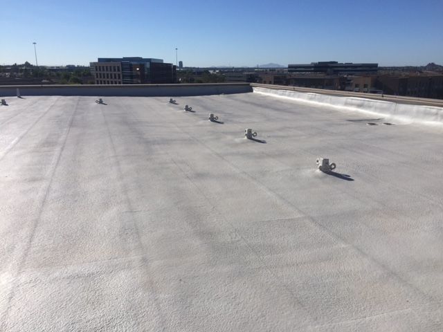 Flat white rooftop with scattered vents under a clear blue sky.