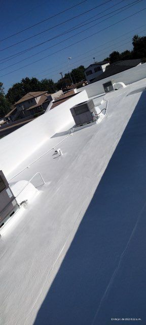 White flat rooftop with HVAC units under a clear blue sky, viewed at an angle.