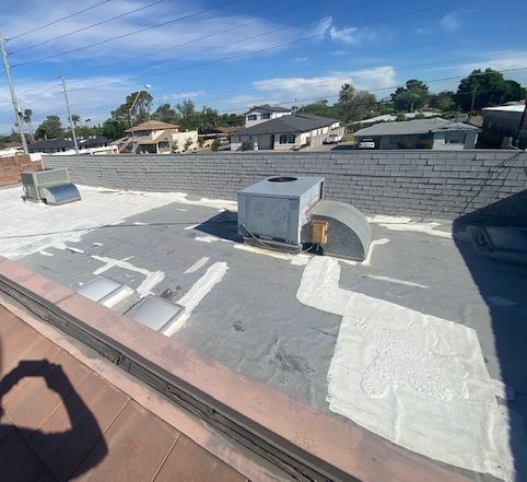 Rooftop with white waterproof coating, vents, and a low brick wall under a clear blue sky.