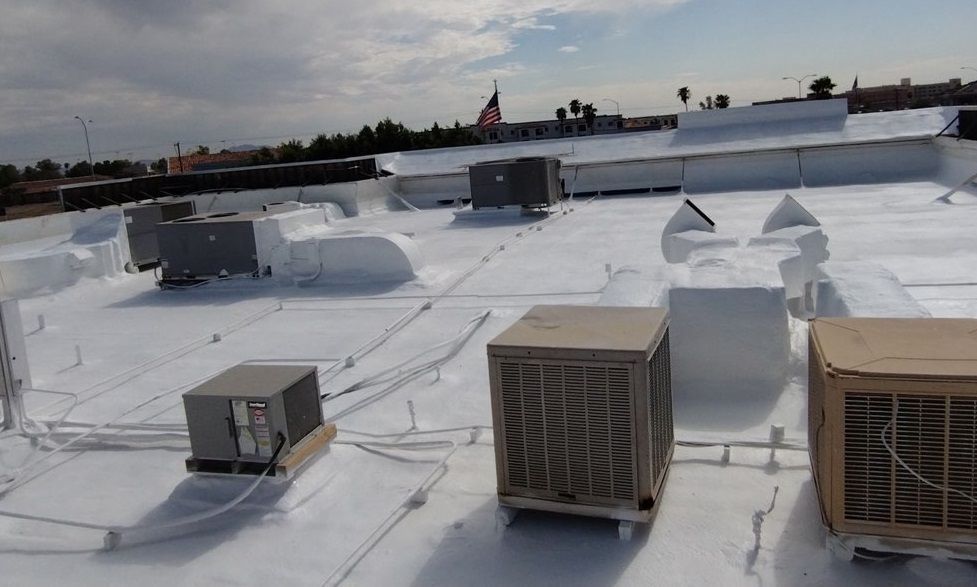White flat rooftop with HVAC units, vents, and pipes under a clear sky.