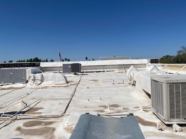 Flat rooftop with white HVAC units, vents, and cables under a clear blue sky.