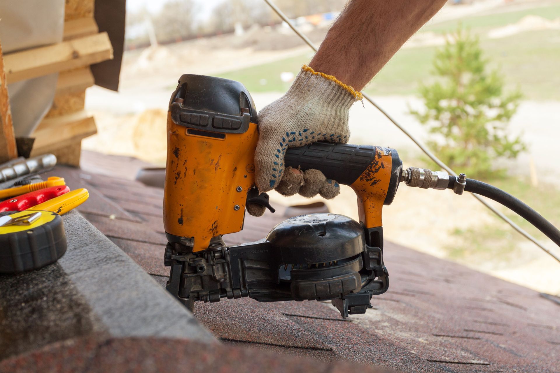 Person using an orange and black nail gun on a wooden surface outdoors