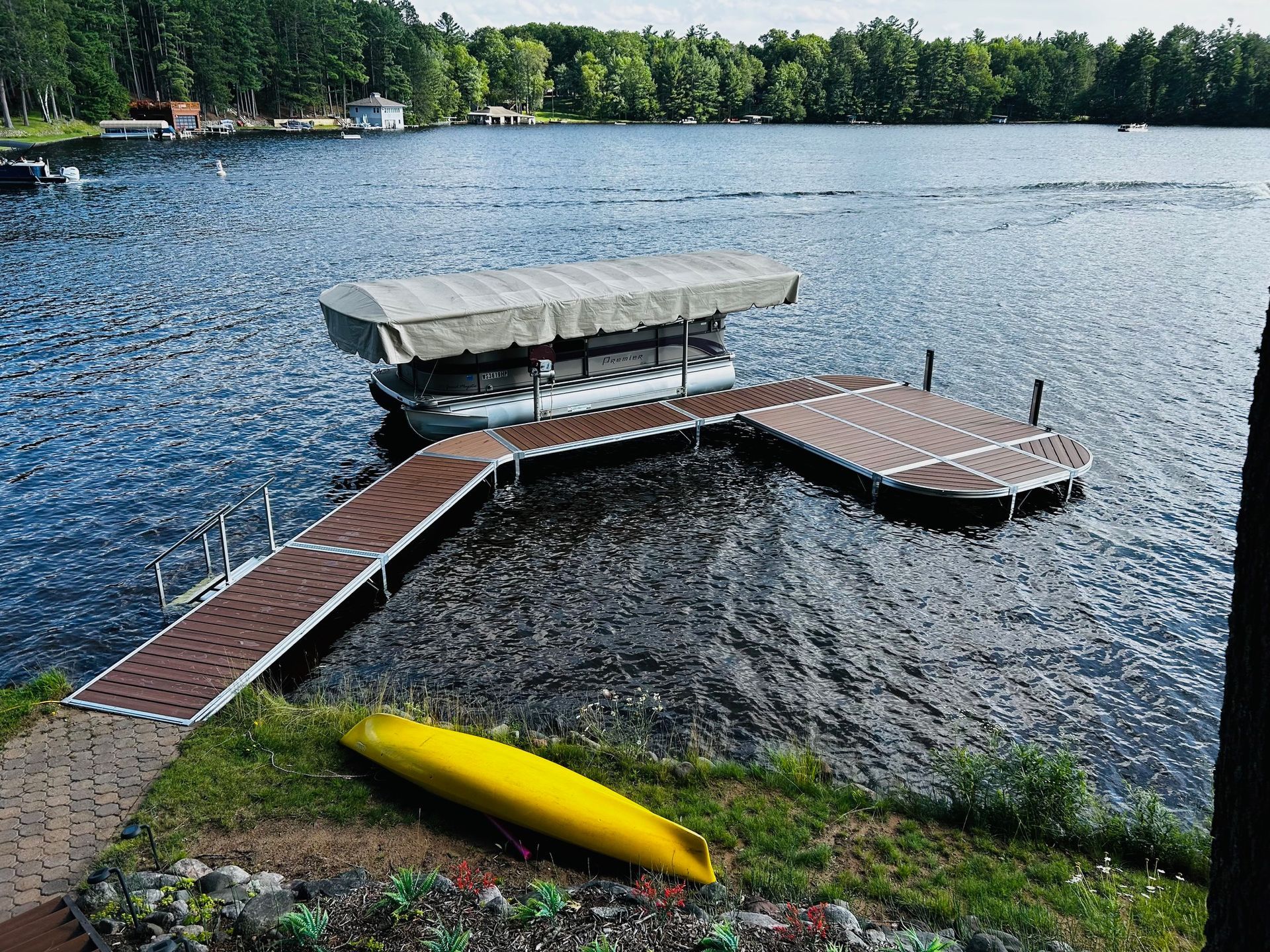 A yellow kayak is sitting on the shore of a lake next to a dock.