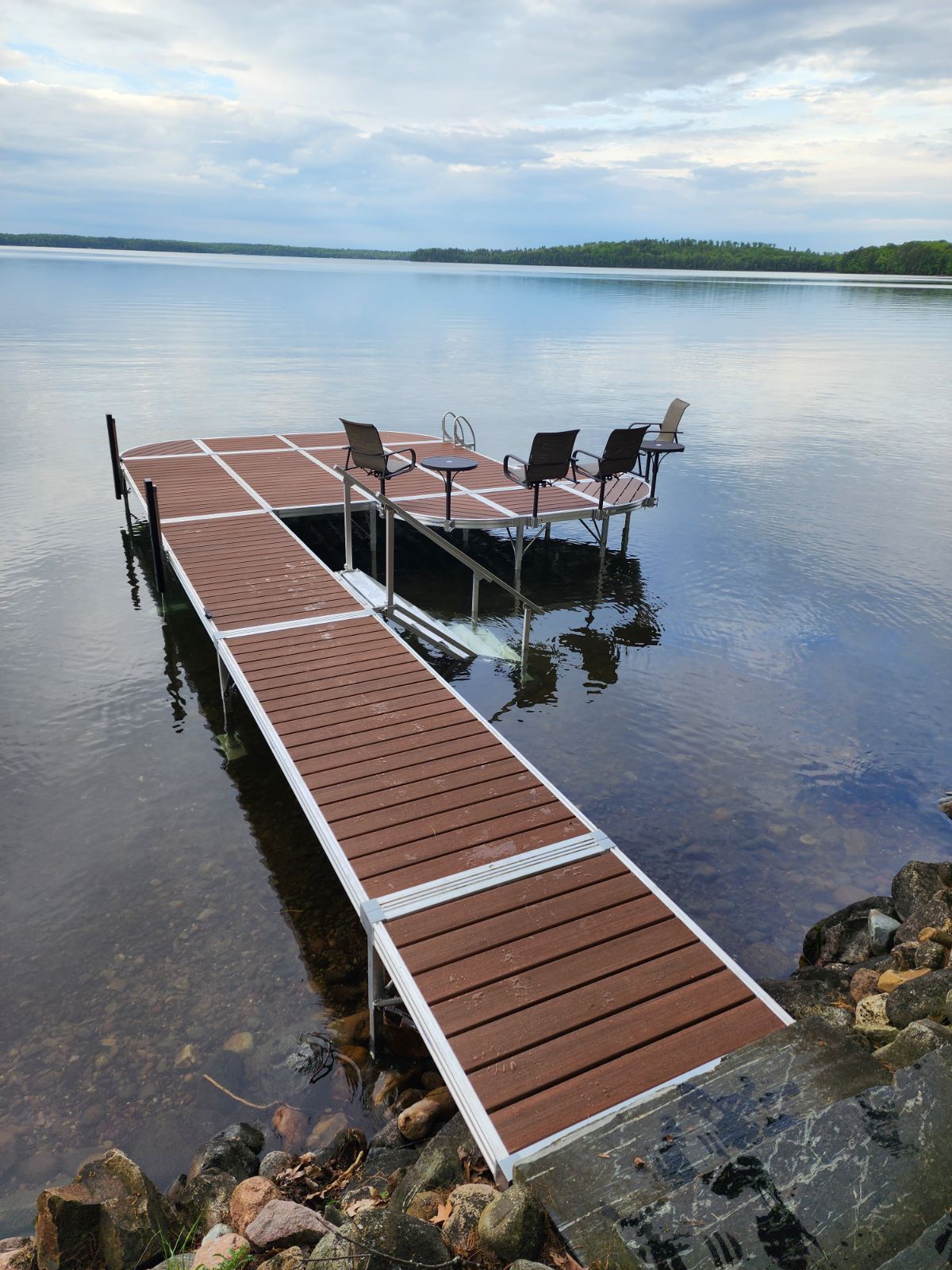 A dock with chairs on it is in the middle of a lake.