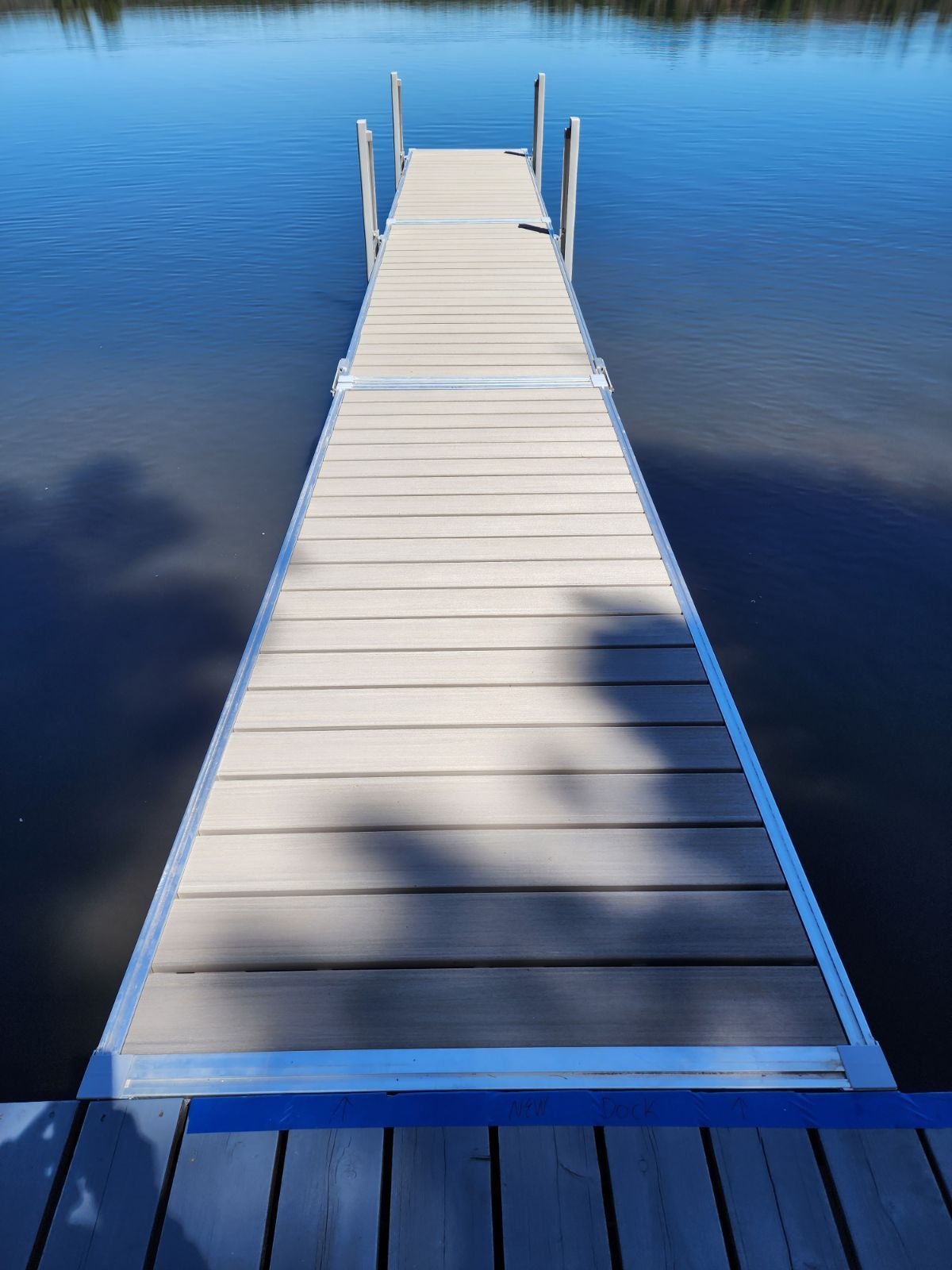 A dock leading into a lake with a tree shadow on it.