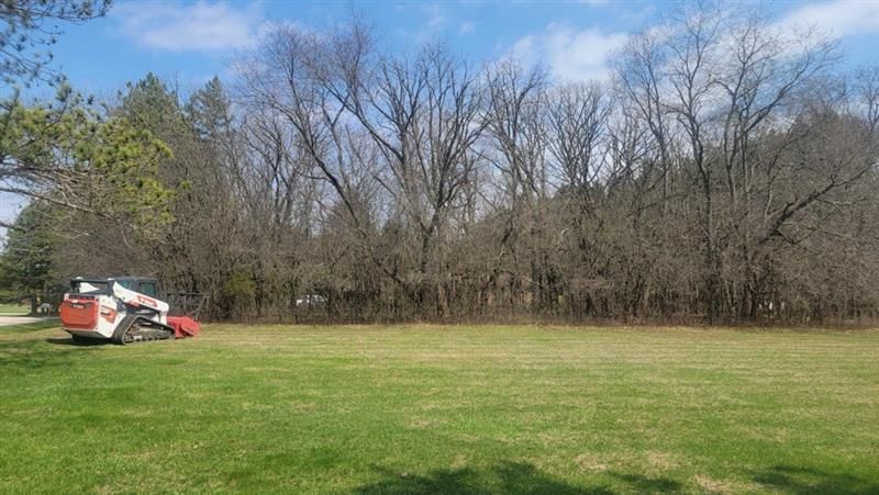 Bobcat mowing green grass in front of trees under a blue sky.