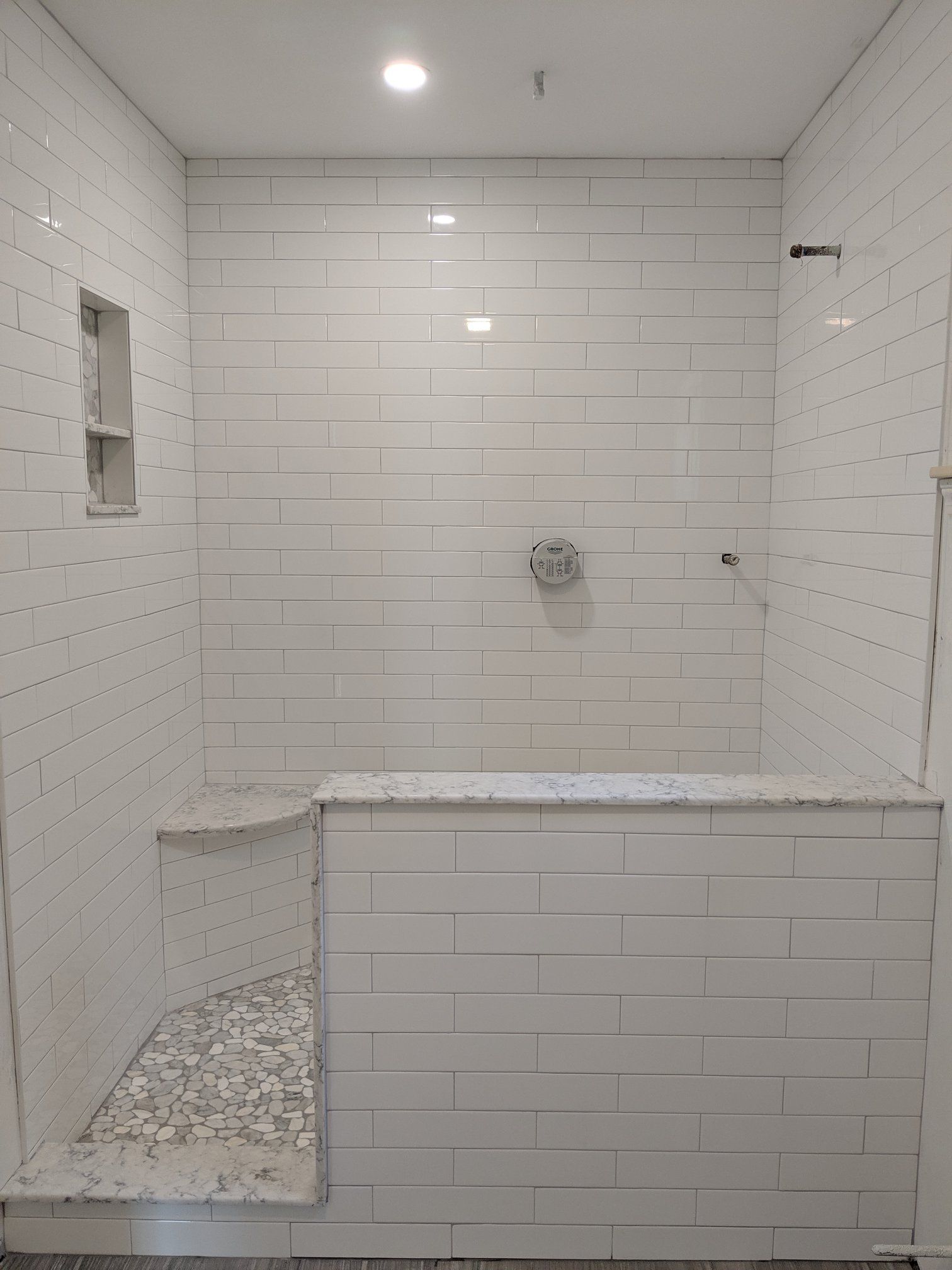 White tiled shower with bench, niche, and pebbled floor.