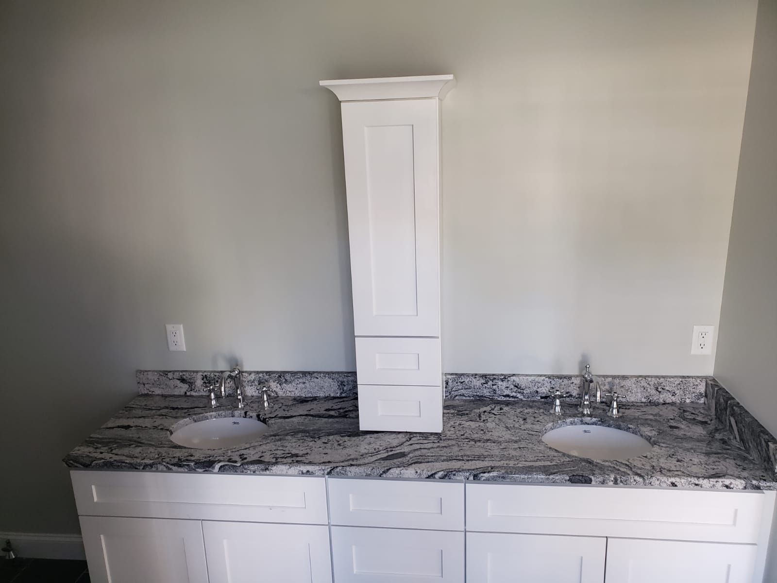 Bathroom vanity with a white cabinet, granite countertop, two sinks, and a tall, matching wall cabinet.