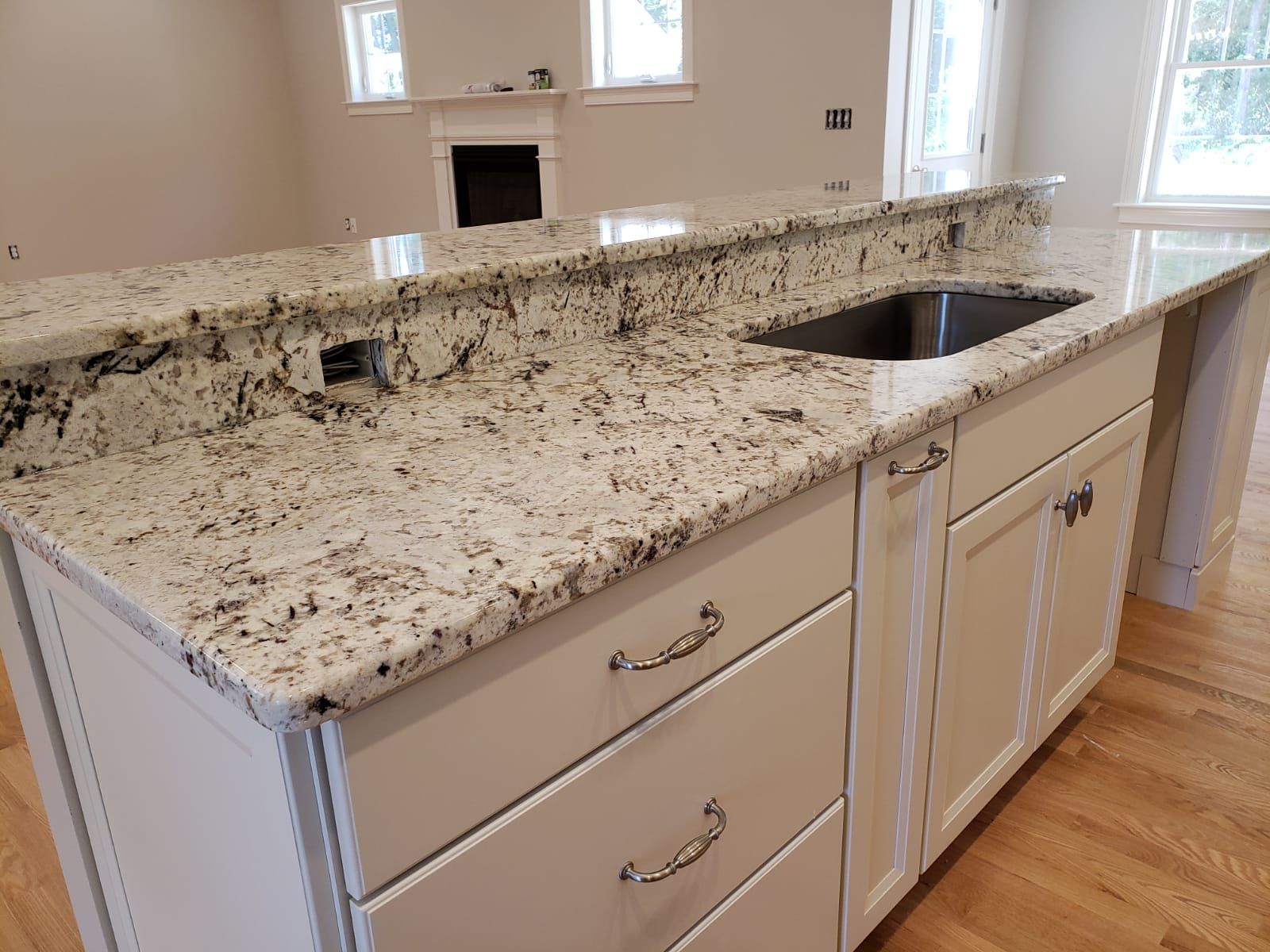 Kitchen island with granite countertop, white cabinets, and stainless steel sink.