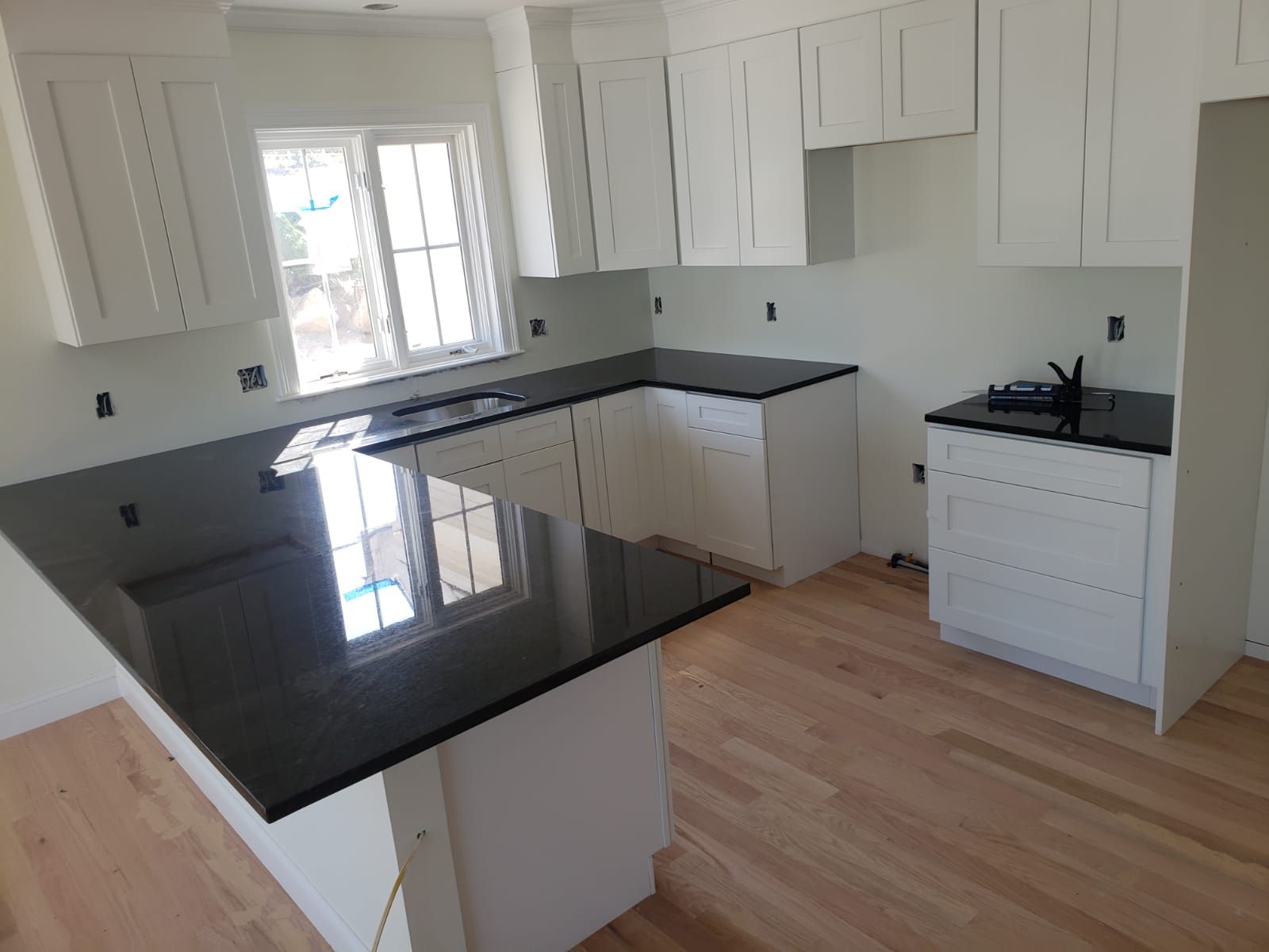 White kitchen cabinets with black countertops and light wood floor.