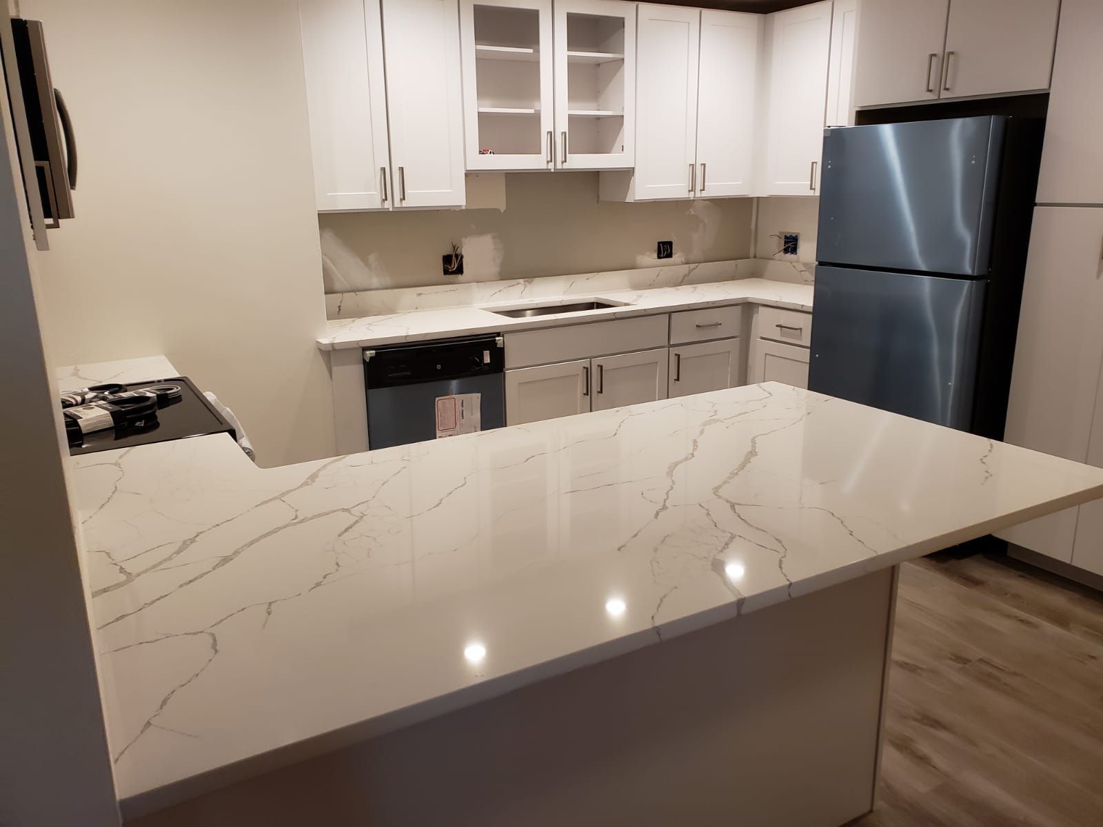 White kitchen with countertop, cabinets, and stainless steel refrigerator.