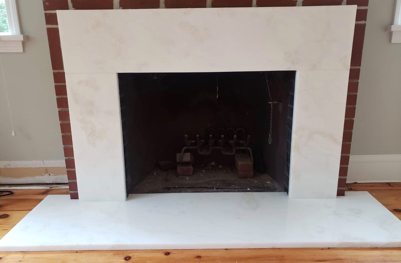Cream-colored fireplace with a brick border and a dark interior, set in a room with wood flooring.