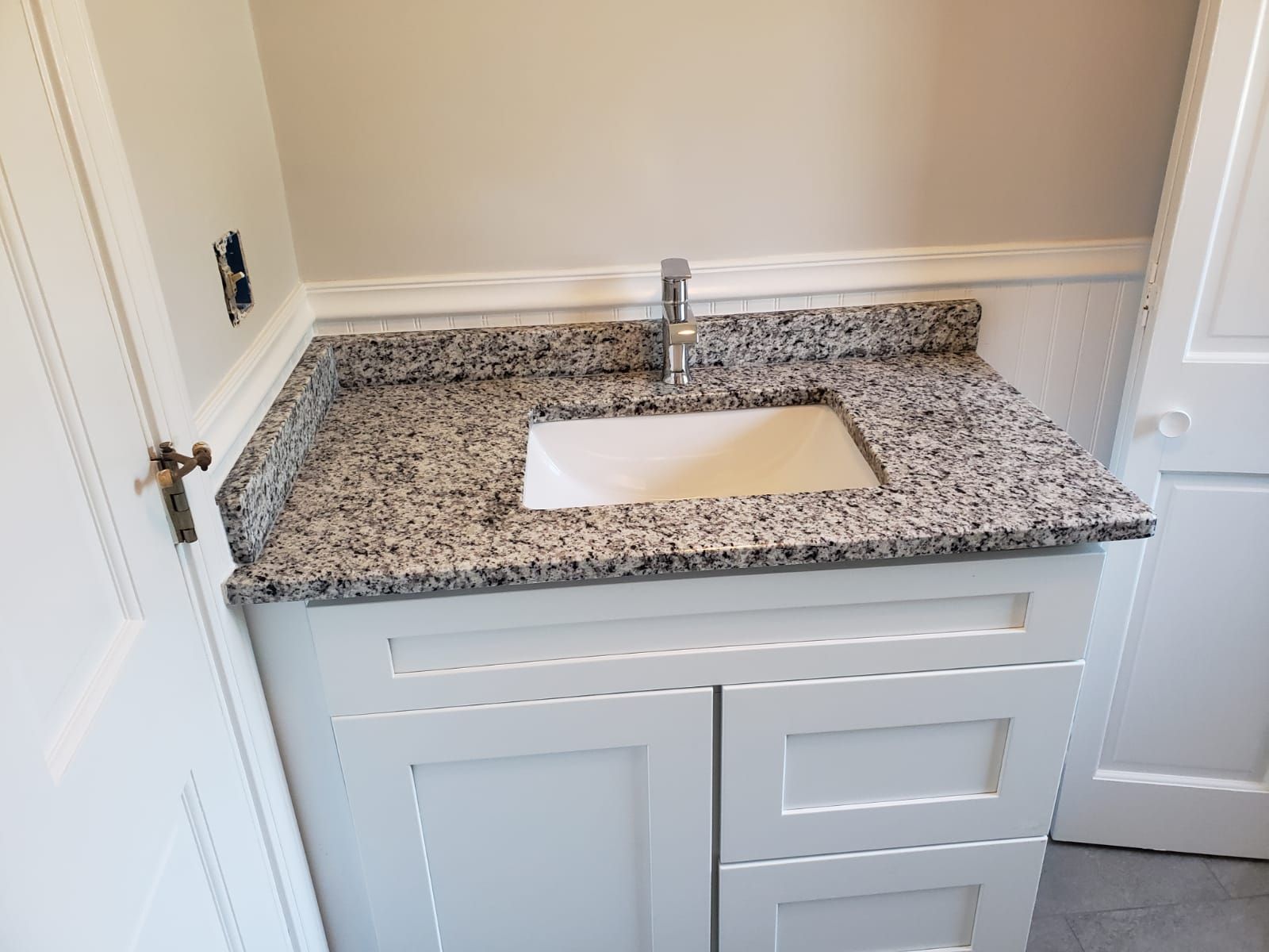 Gray granite countertop with white sink on a white cabinet in a bathroom.