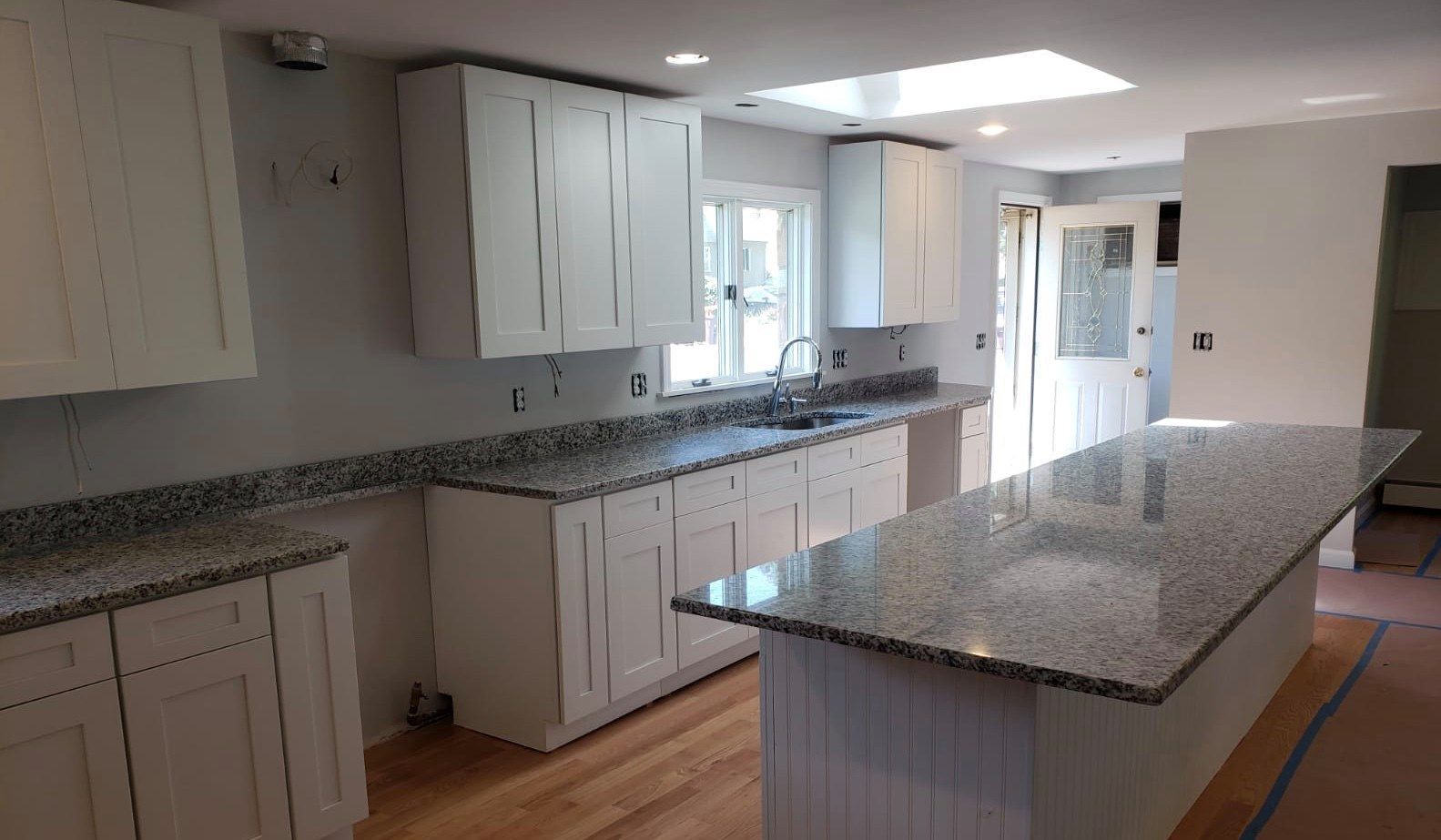 White kitchen with granite countertops and island, skylight, and light wood floor.