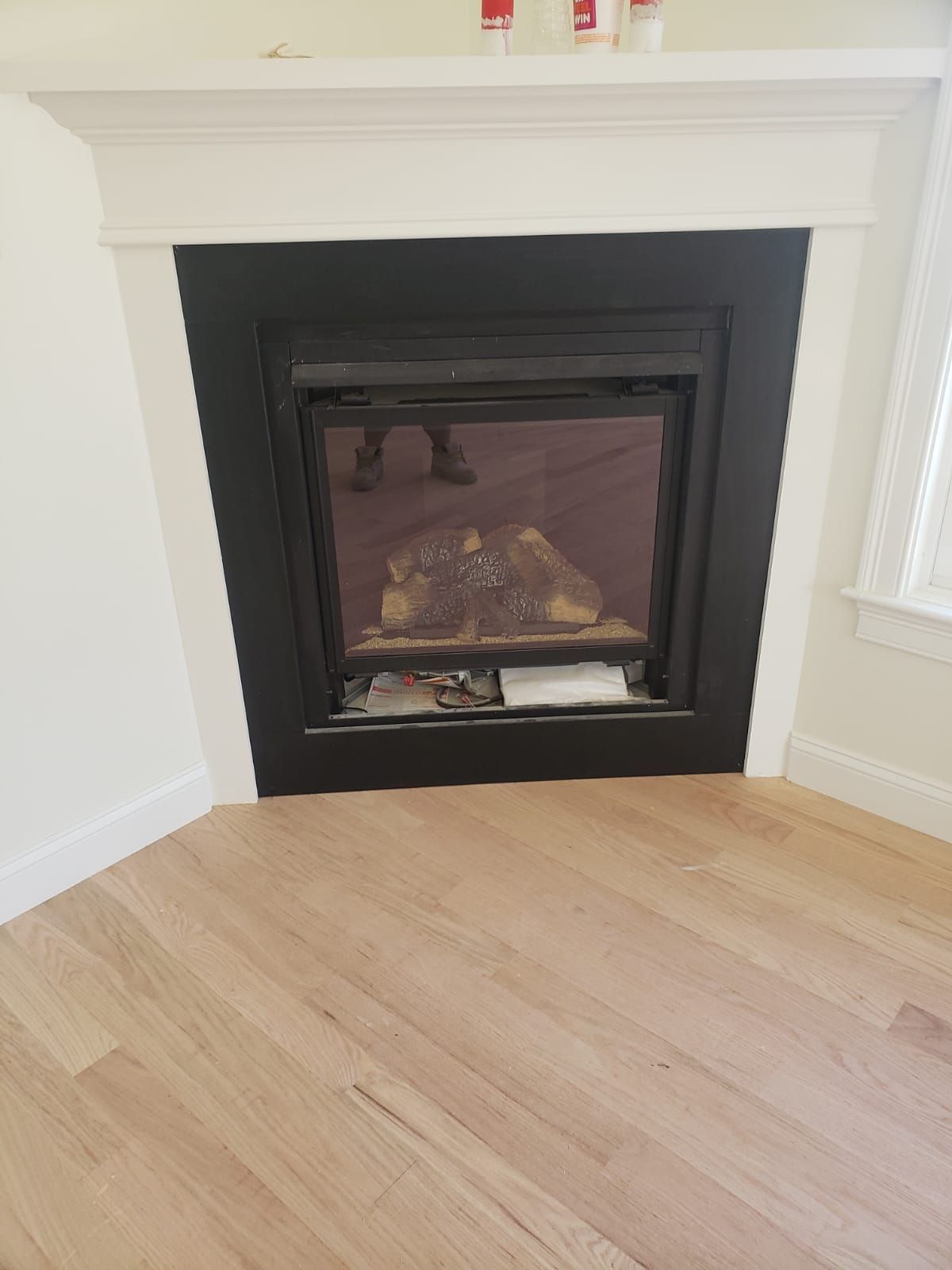 Fireplace set in a corner, surrounded by white trim and wooden floor.