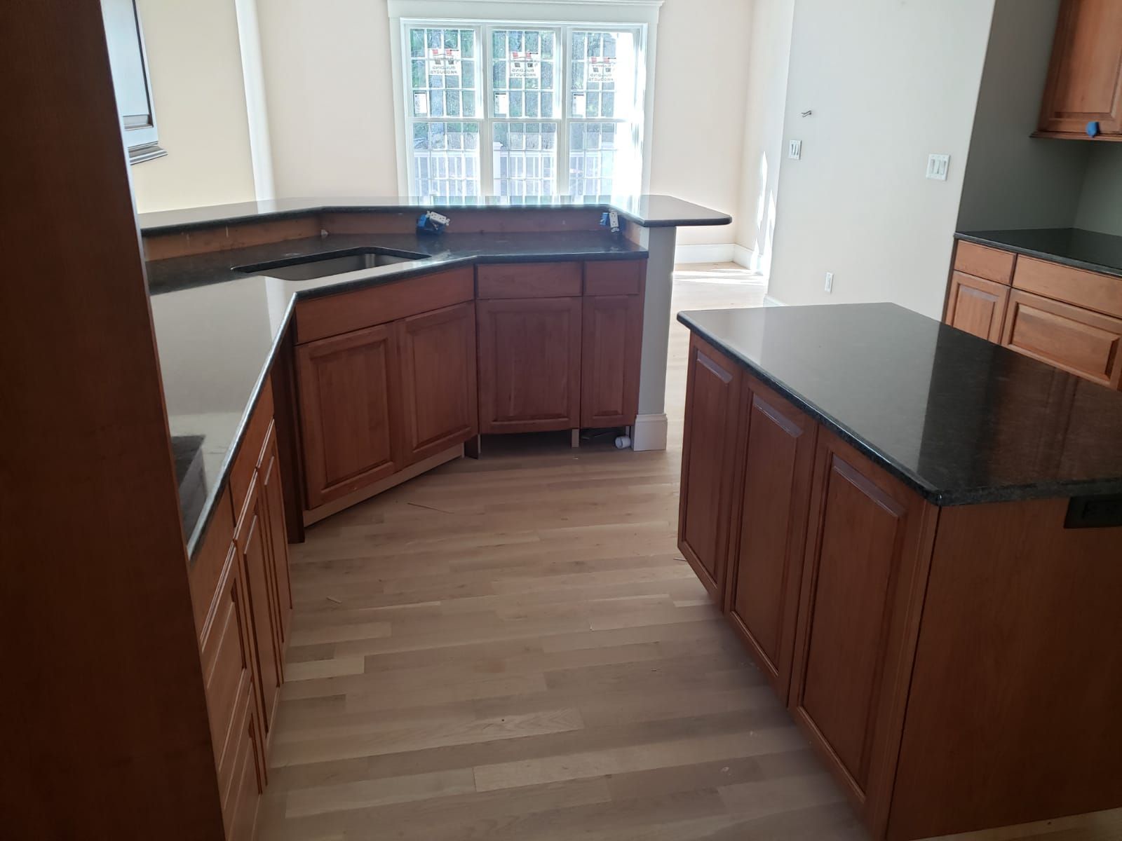 Kitchen with wooden cabinets, black countertops, and a center island, light wood floors.