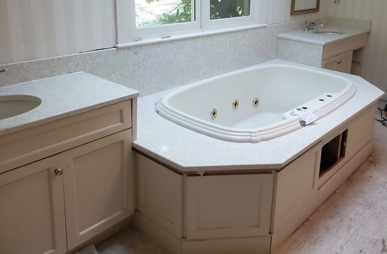 Bathroom with white cabinets, jacuzzi tub, and countertop, next to a window.