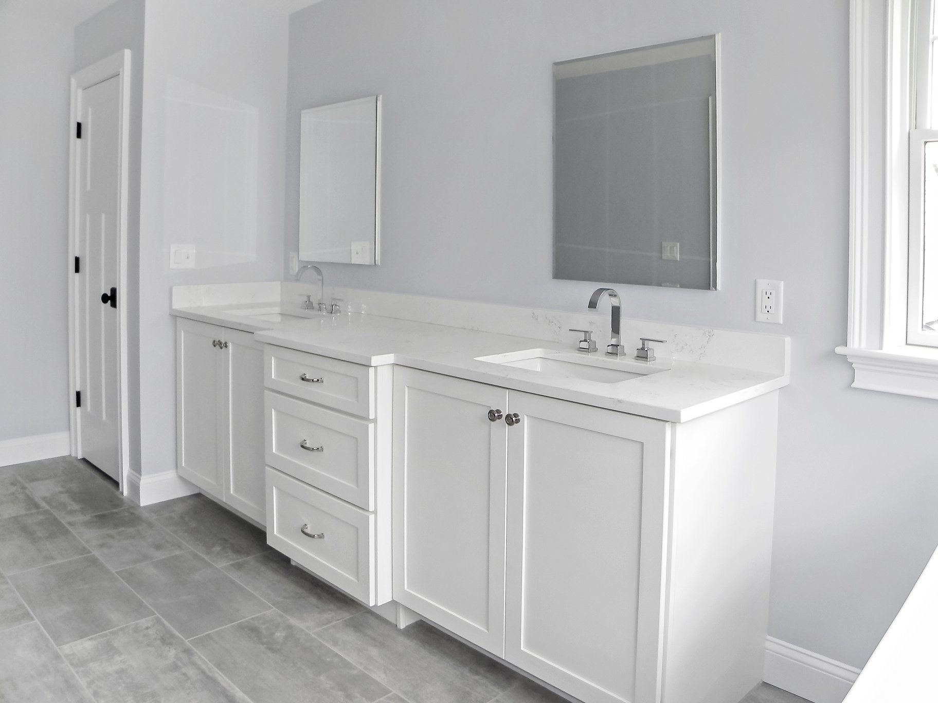 White double vanity in a bathroom with gray walls, mirrors, and a door.