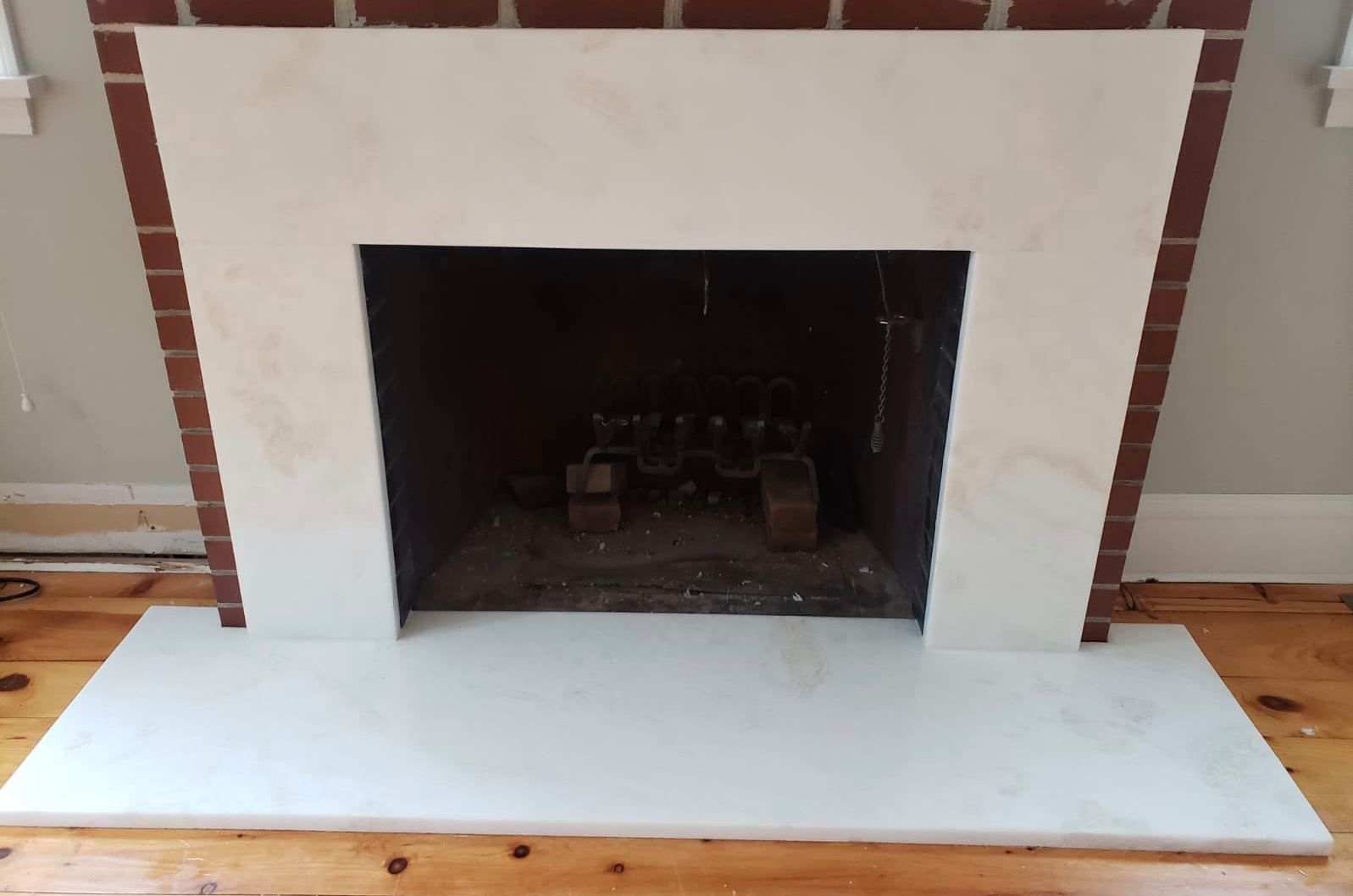 Fireplace with a white stone facade and hearth against red brick.
