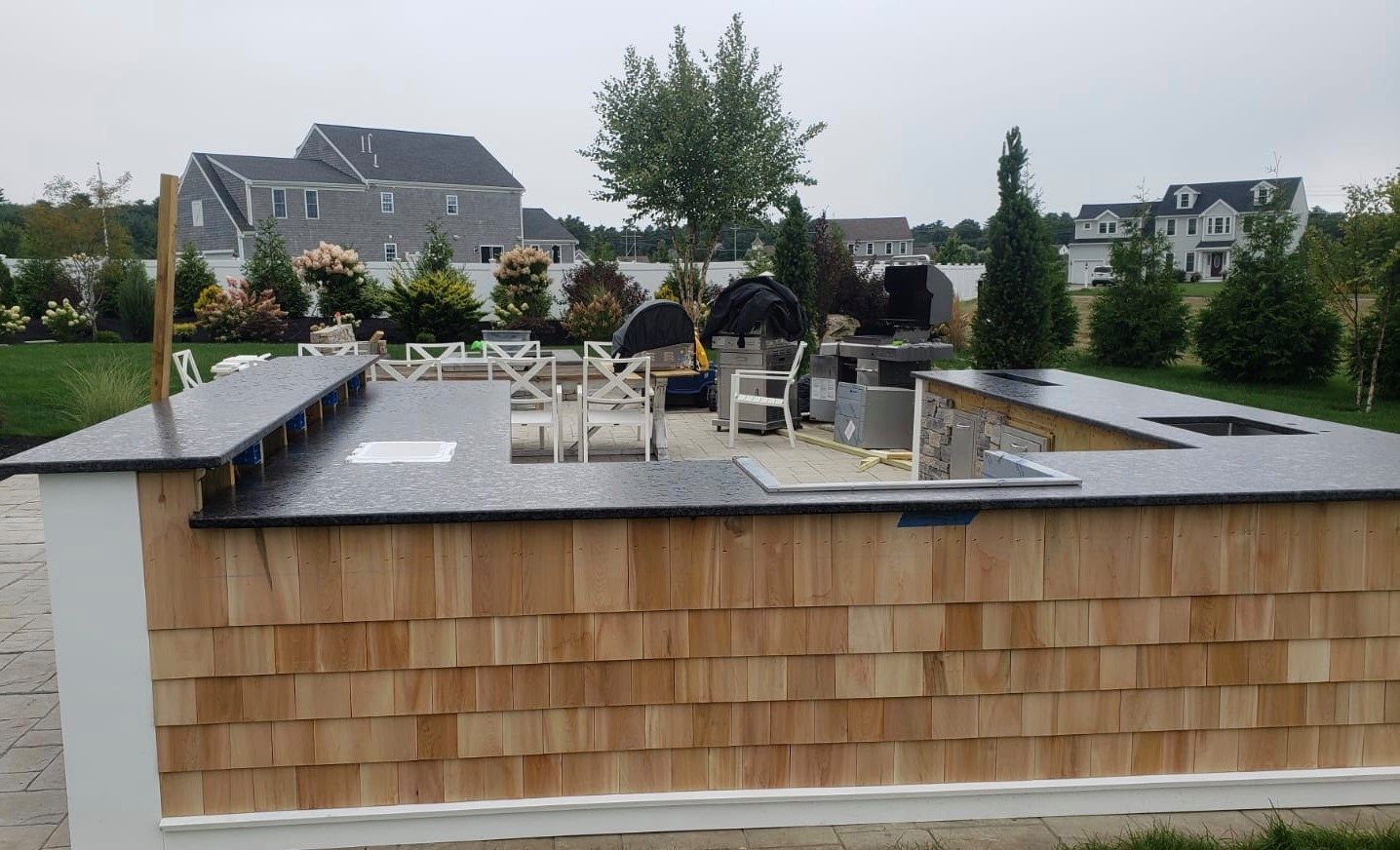 Outdoor kitchen with cedar siding, dark countertops, and stainless steel appliances on a patio.