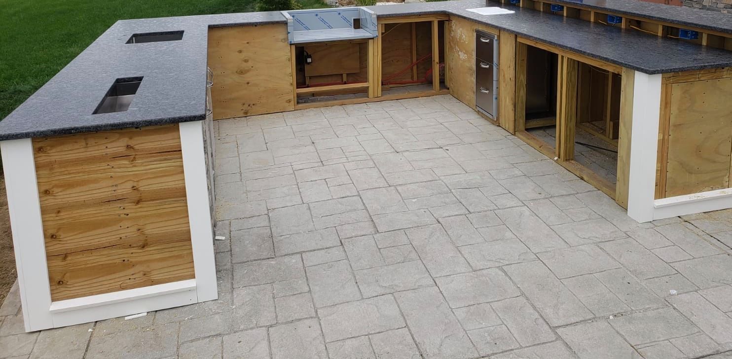 Outdoor kitchen with dark countertop and wood structure on a paved patio.