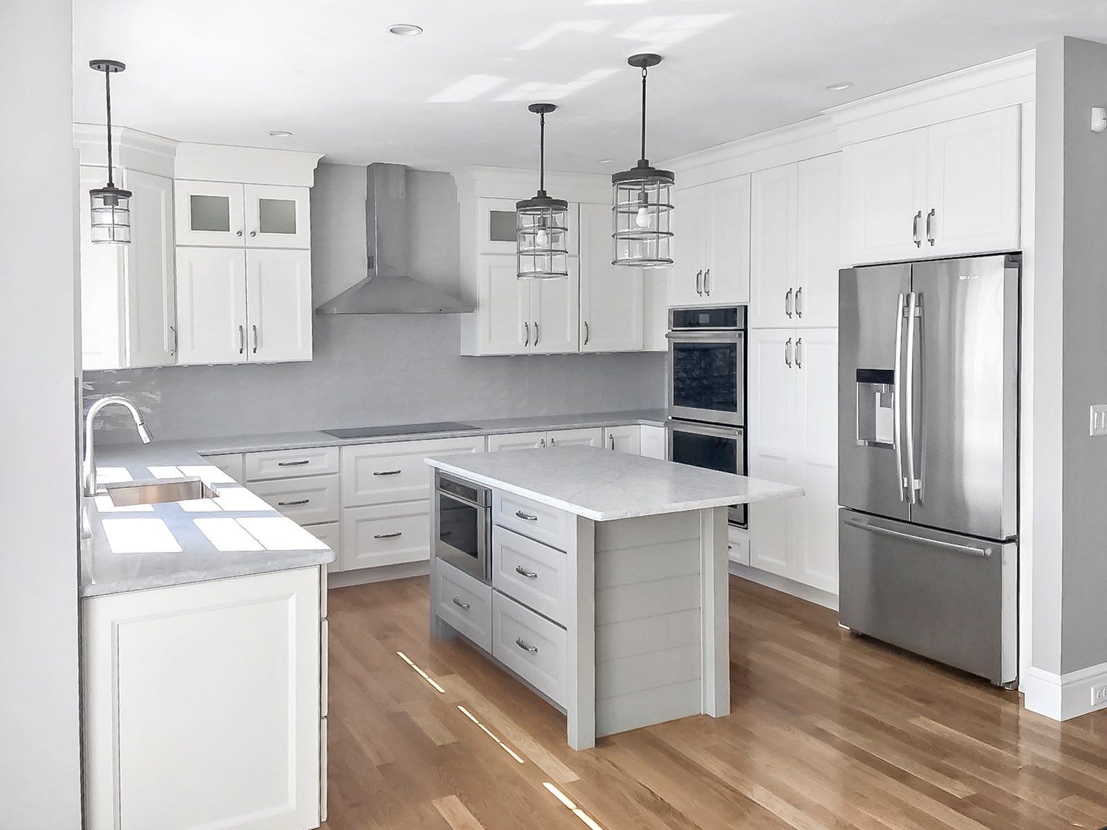 Bright white kitchen with island, stainless steel appliances, and wooden floors.