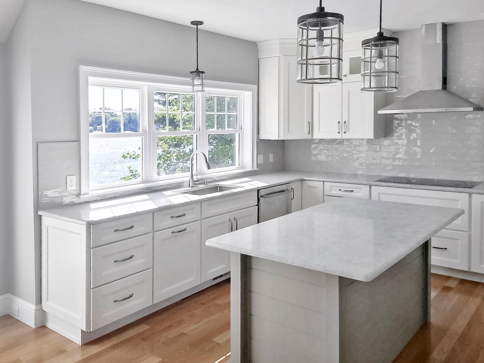 White kitchen with island, cabinets, stainless appliances, and large windows overlooking a body of water.