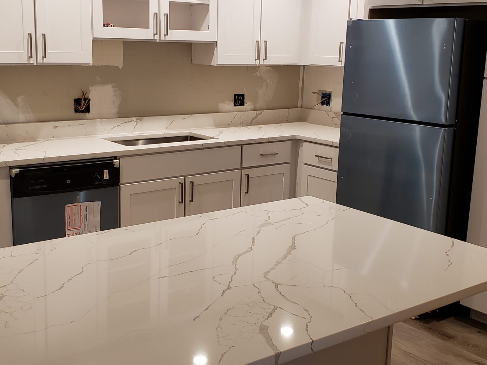 Modern kitchen with white cabinets, quartz countertops, island, and stainless steel refrigerator.