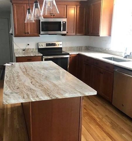 Kitchen with brown cabinets, island with patterned countertop, stainless steel appliances, and hardwood floors.