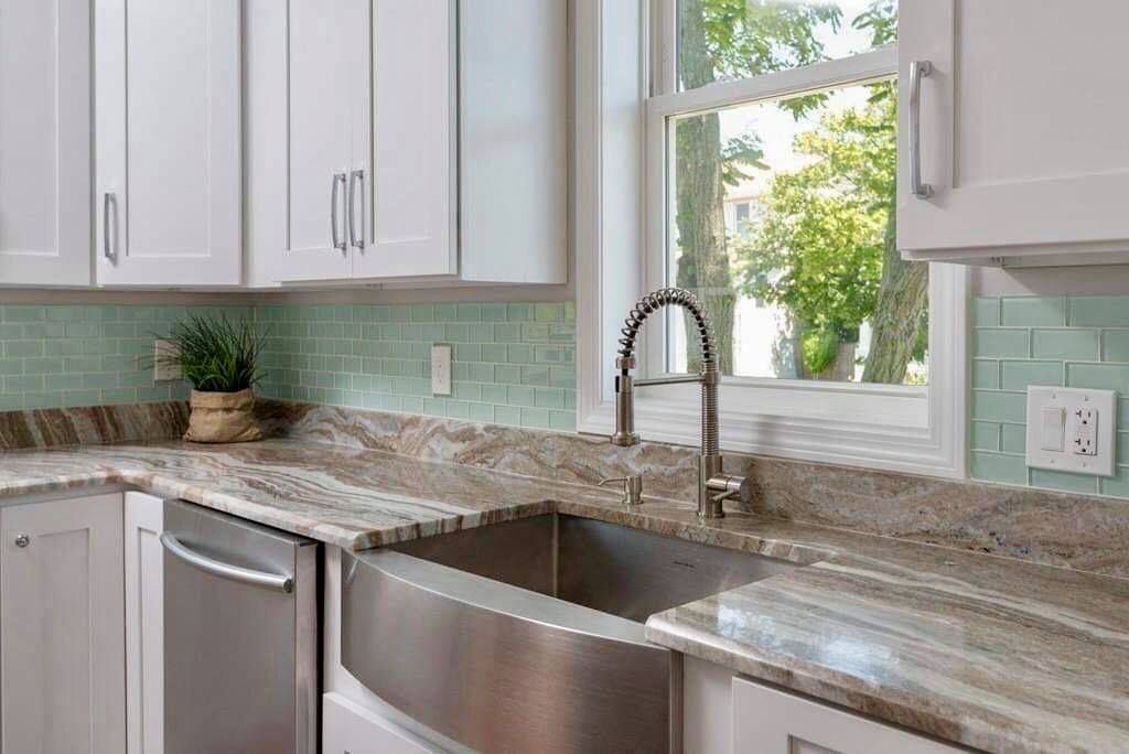 Kitchen with white cabinets, stainless steel sink, granite countertops, and a window overlooking greenery.