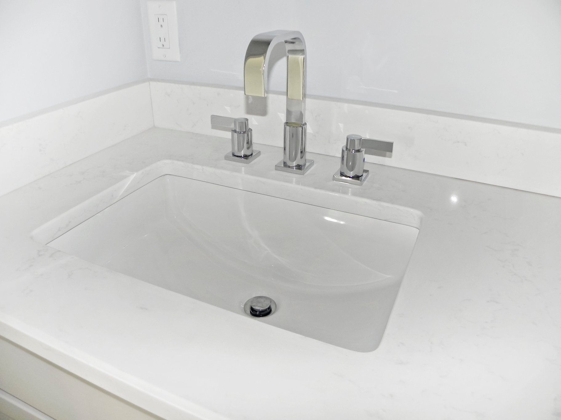 White bathroom sink with chrome faucet and handles on a white countertop.