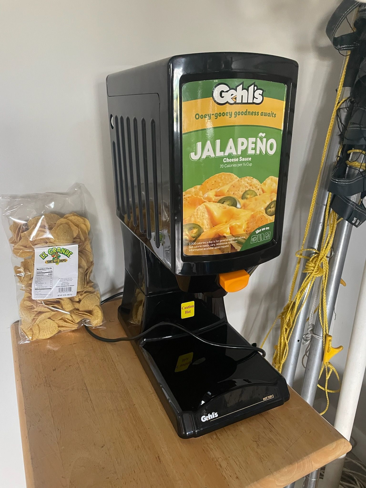 A jalapeno dip dispenser is sitting on a wooden table next to a bag of chips.