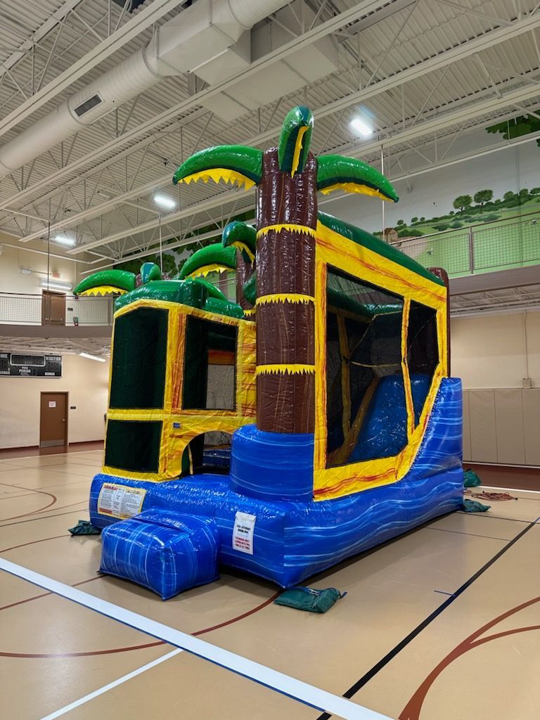 A large bouncy house with palm trees on top of it is in a gym.