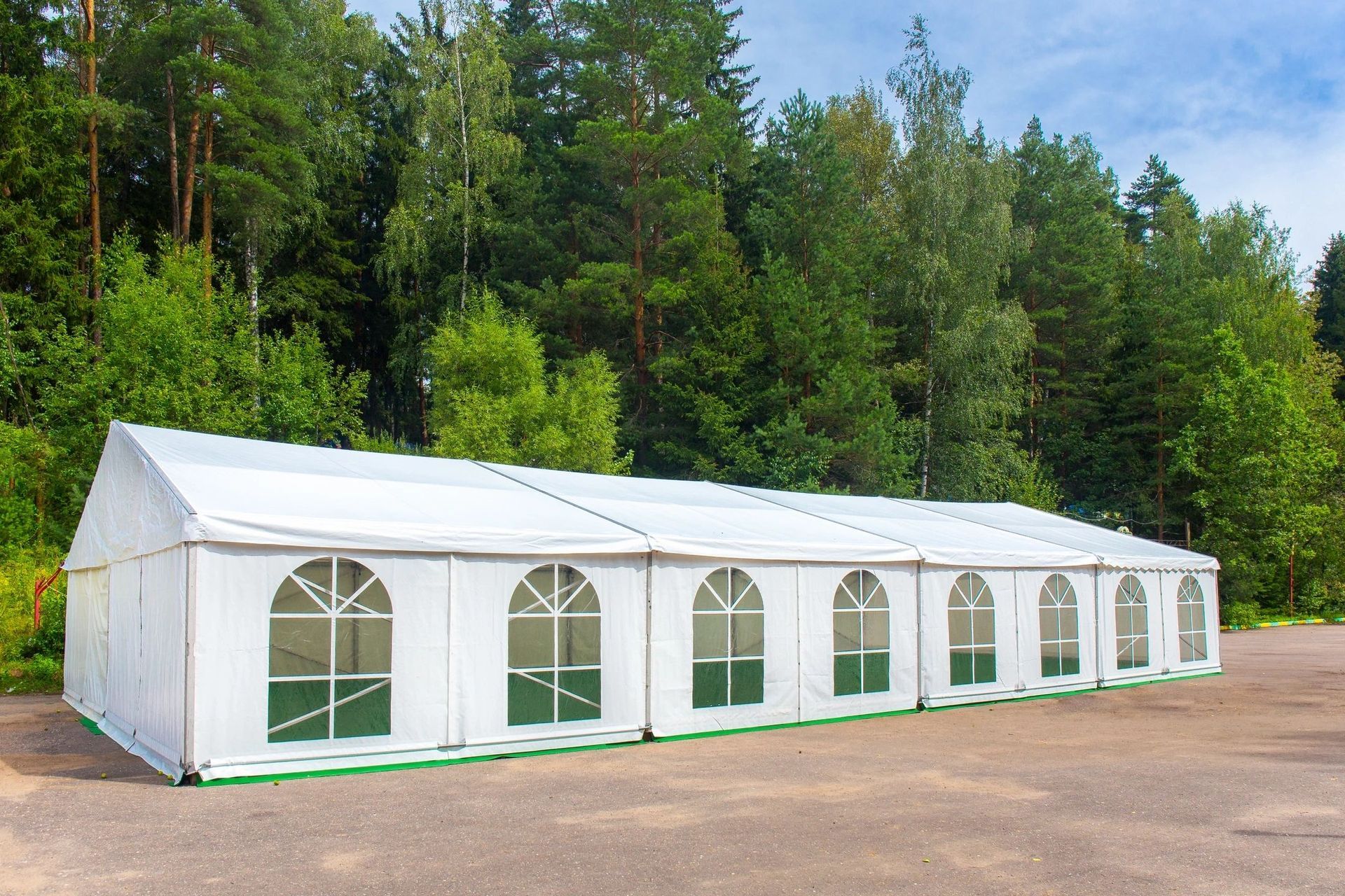 A large white tent is sitting in a parking lot in front of a forest.