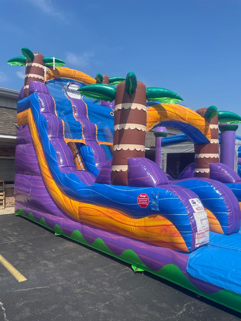 A large inflatable water slide with palm trees is sitting in a parking lot.