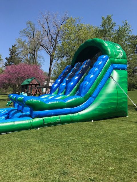 A green and blue inflatable water slide is sitting on top of a lush green field.