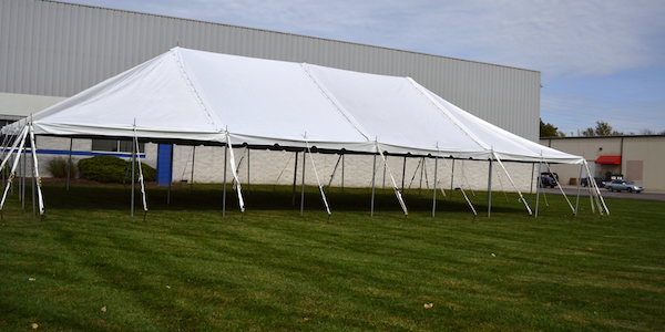 A large white tent is sitting in the grass in front of a building.