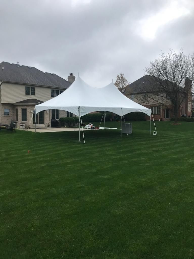 A white tent is sitting in the middle of a lush green field in front of a house.