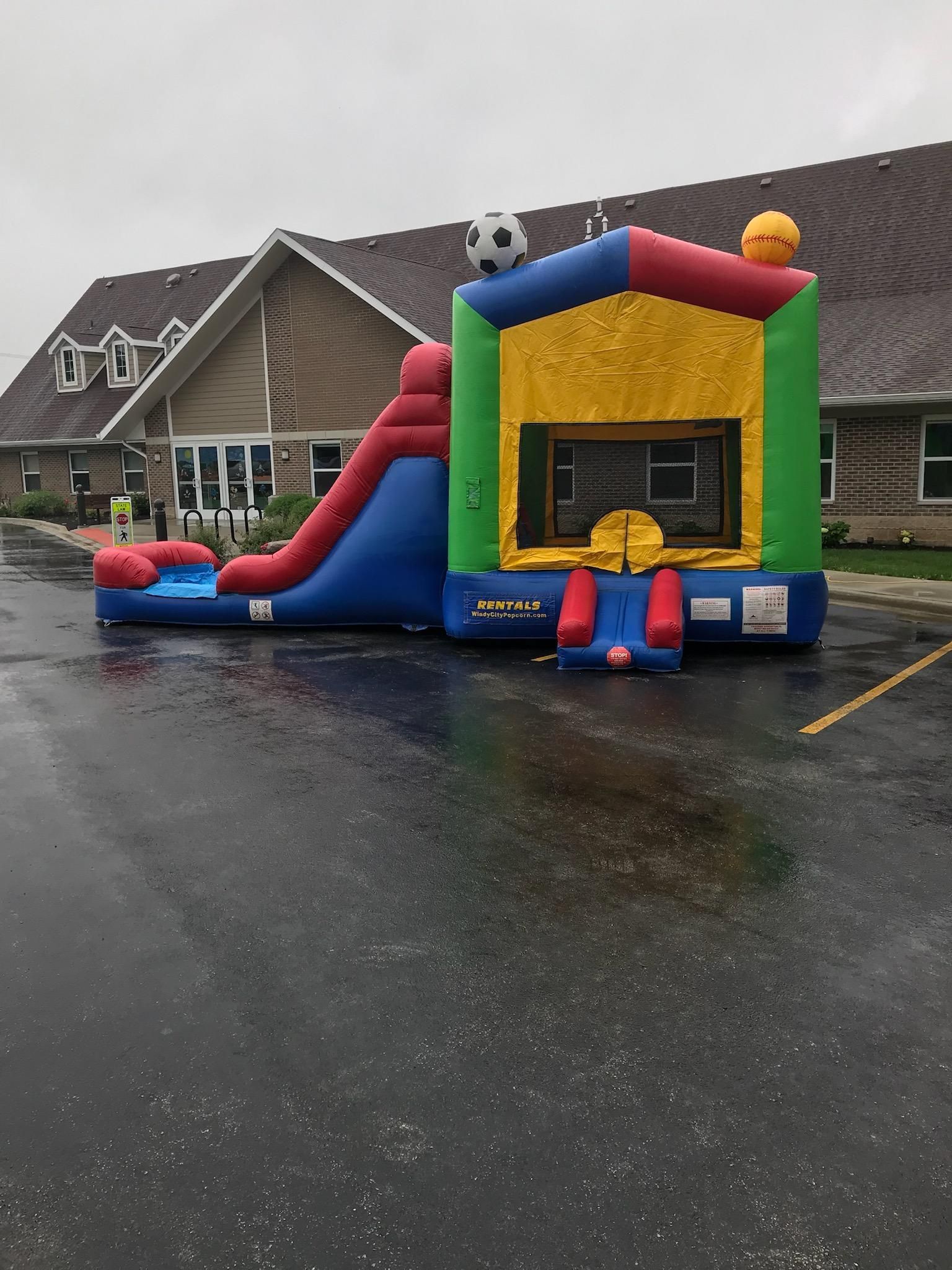 A bouncy house with a slide is in a parking lot in front of a building.