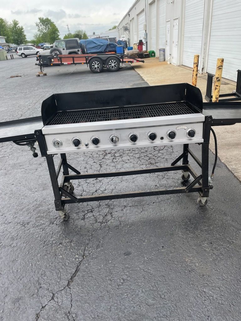 A grill is sitting in a parking lot next to a trailer.