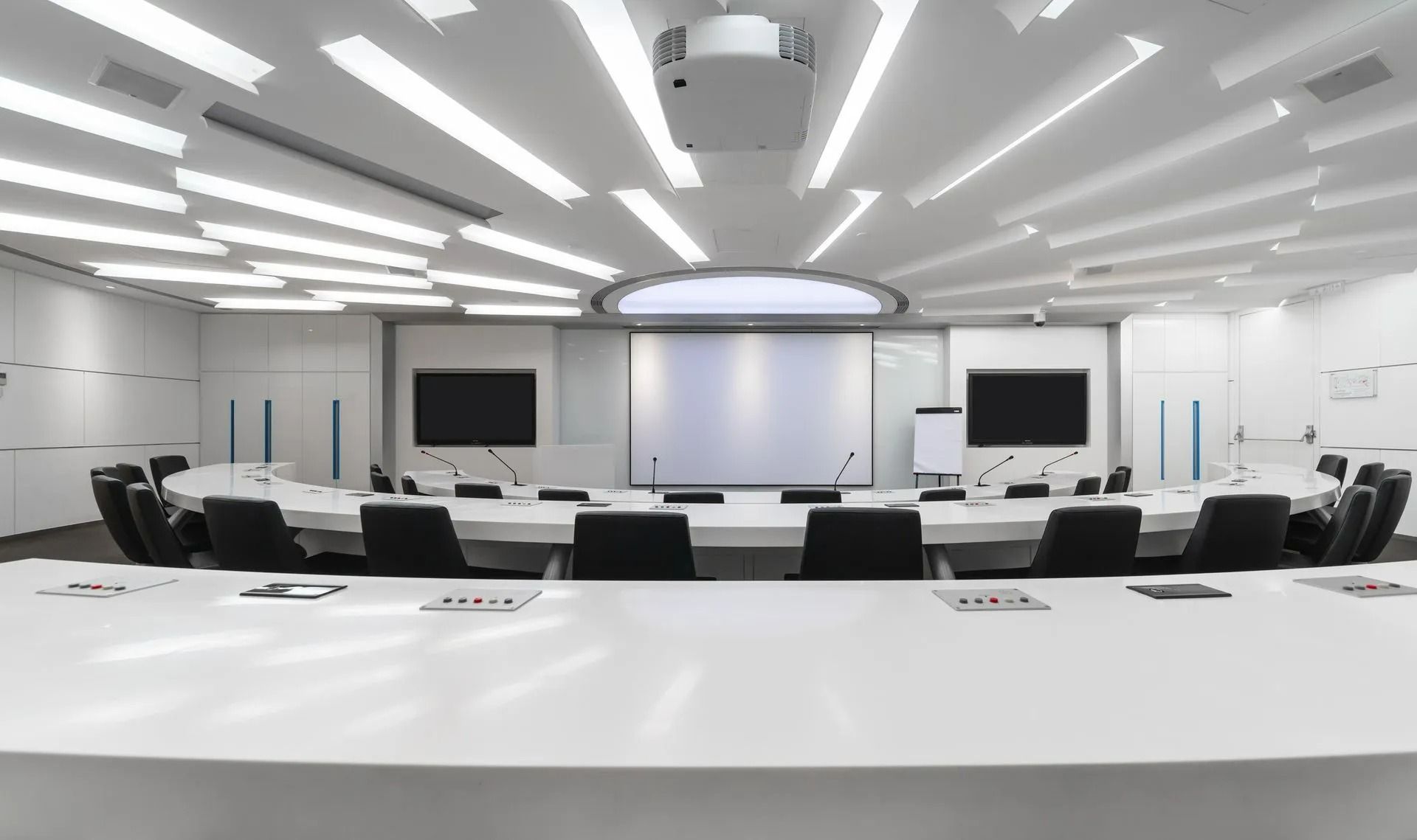 Empty modern conference room with white tables, black chairs, and projector screens at the front